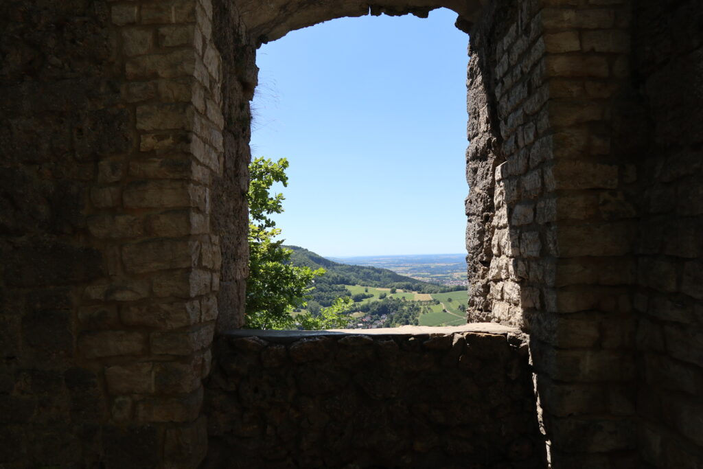 A photo inside ruins of a castle looking out throw a window into a sunny landscape.